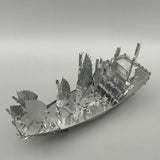 Het Schatschip van Zheng He Metalen Bouwpakket - Chinees Jonk Model van SlimSpul nederland b.v., een zilveren metalen model met meerdere zeilen en fijne details, ligt op een grijze achtergrond-ideaal voor liefhebbers van metalen bouwpakketten.