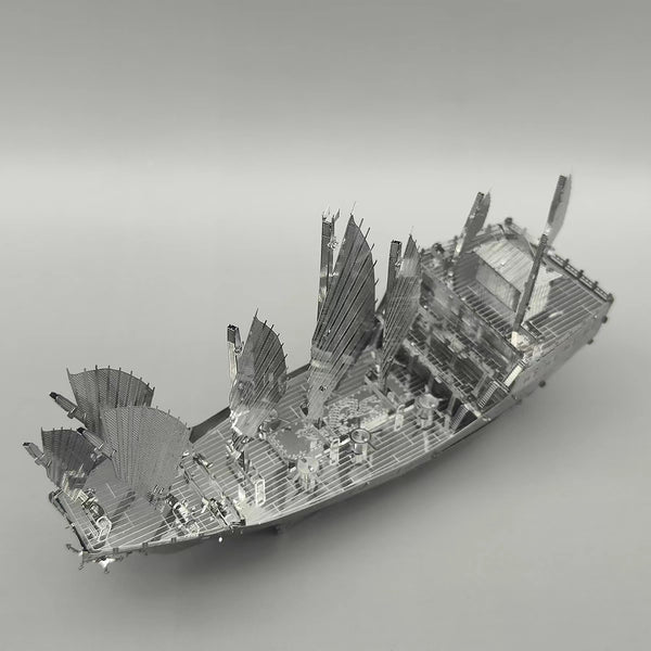 Het Schatschip van Zheng He Metalen Bouwpakket - Chinees Jonk Model van SlimSpul nederland b.v., een zilveren metalen model met meerdere zeilen en fijne details, ligt op een grijze achtergrond-ideaal voor liefhebbers van metalen bouwpakketten.