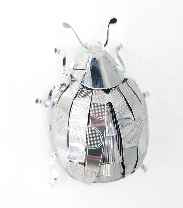 Een glanzend Lieveheersbeestje Metalen Bouwpakket van SlimSpul nederland b.v. heeft gegraveerde patronen en gebogen poten, gefotografeerd op een witte achtergrond.