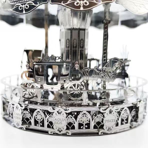 De Draaimolen met Sterrenbeelden Metalen Bouwpakket - Kermis Attractie van SlimSpul nederland b.v. is een zilveren carrouselmodel met koets en eenhoorn, voorzien van Waterman en Vissen gravures in een sierlijk, reflecterend ontwerp.