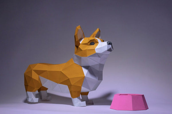 Het Corgi met Voerbakje 3D Papier Model van SlimSpul nederland b.v. toont een polygonale Corgi naast een roze hondenvoerbak op een grijze achtergrond - ideaal bouwpakket voor papercraftliefhebbers.