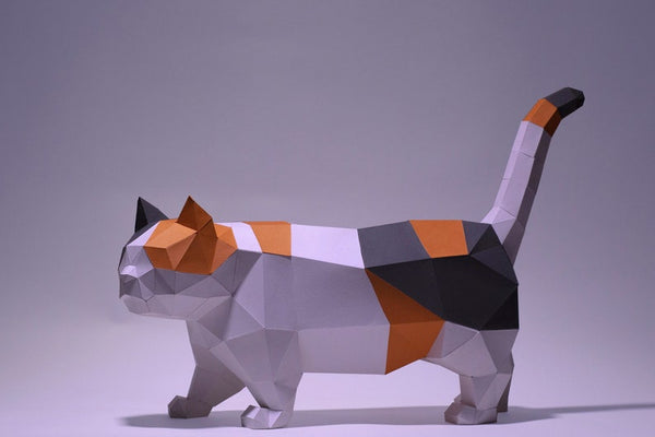 De Munchkin Kat 3D Papier Model van SlimSpul nederland b.v. is een geometrische, low-poly DIY sculptuur van een kortbenige kat (Raskat met Korte Pootjes) in calico kleuren, staand op handen en voeten met zijn staart omhoog.