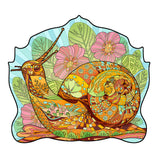 Een levendige slak met een gebloemde schelp rust tussen roze bloemen en groene bladeren op blauw, zoals te zien is in de Slak Houten Puzzel (A4+ formaat) - Unieke Tuinbewoner Figuurpuzzel van SlimSpul nederland b.v.- perfect voor legpuzzel fans.